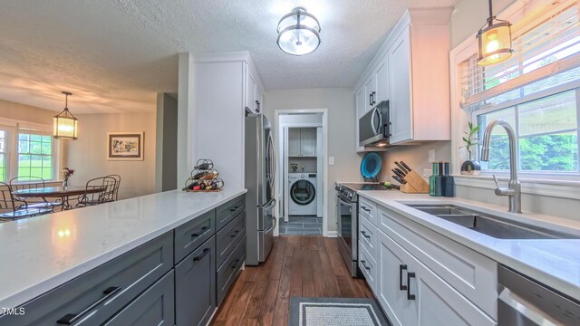 kitchen with washer / dryer, appliances with stainless steel finishes, a sink, white cabinets, and hanging light fixtures