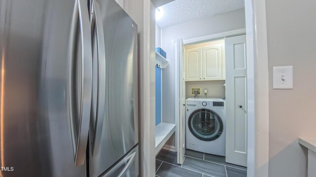 washroom with washer / clothes dryer, cabinet space, a textured ceiling, and dark tile patterned flooring