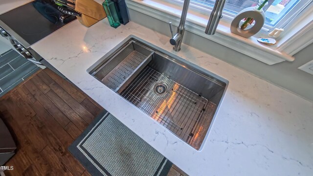 kitchen view of a sink, stone countertops, and wood finished floors