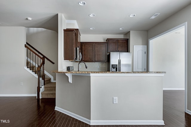 kitchen featuring appliances with stainless steel finishes, light stone counters, dark brown cabinets, dark wood-type flooring, and a peninsula