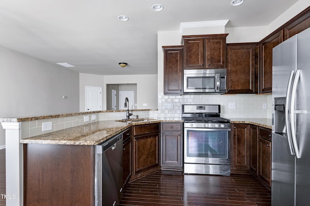 kitchen featuring stainless steel appliances, a sink, a peninsula, light stone countertops, and dark brown cabinetry