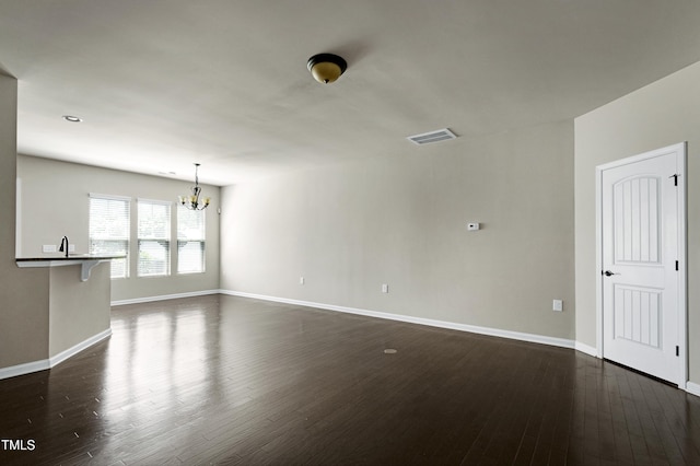 unfurnished living room featuring a chandelier, dark wood-type flooring, and baseboards