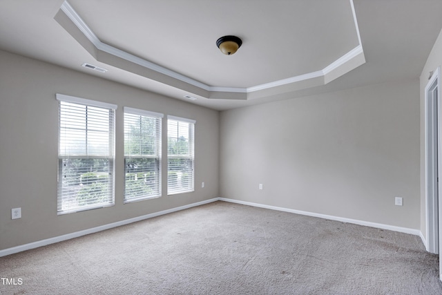 empty room with a tray ceiling, crown molding, carpet floors, and baseboards
