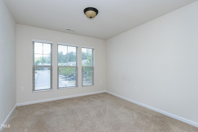 spare room featuring light colored carpet and baseboards