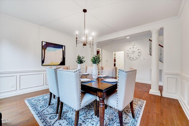 dining area featuring a chandelier, wood finished floors, ornamental molding, wainscoting, and a decorative wall