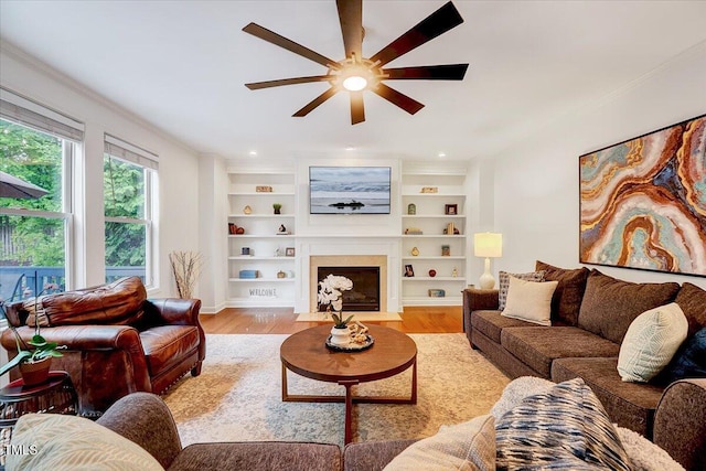 living room with ceiling fan, ornamental molding, light wood finished floors, and a fireplace with flush hearth