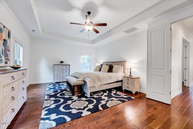 bedroom featuring a tray ceiling, dark wood-style flooring, baseboards, ceiling fan, and ornamental molding