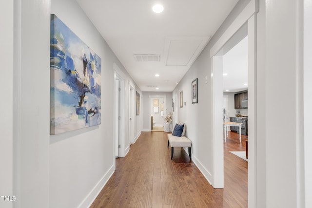 hallway with attic access, wood finished floors, baseboards, and recessed lighting