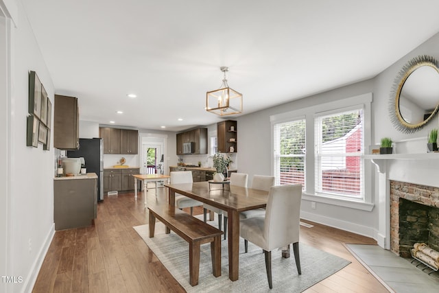 dining space featuring baseboards, recessed lighting, healthy amount of natural light, a stone fireplace, and wood finished floors
