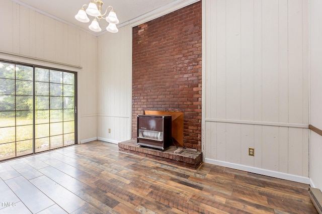 unfurnished living room featuring wood-type flooring, a chandelier, baseboards, ornamental molding, and a wood stove