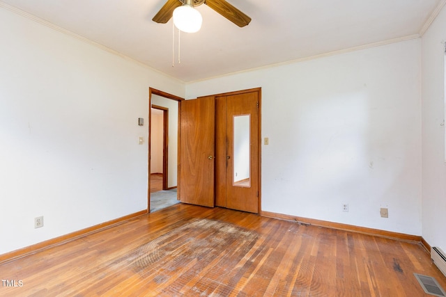 empty room with wood-type flooring, ceiling fan, ornamental molding, baseboards, and a baseboard heating unit