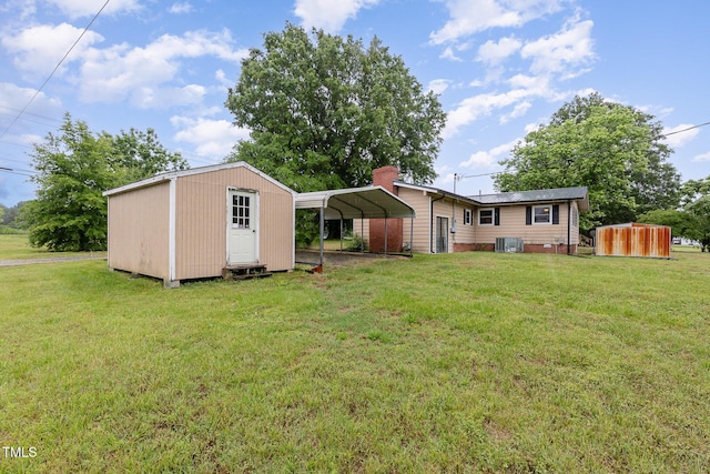 rear view of property featuring a storage unit, a carport, a lawn, and an outbuilding