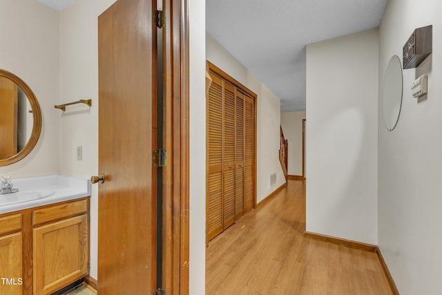 hallway featuring a sink, light wood-style flooring, and baseboards