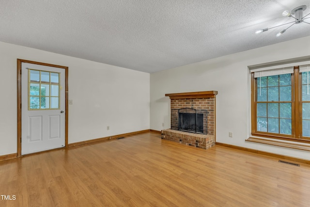 unfurnished living room featuring a textured ceiling, light wood finished floors, healthy amount of natural light, baseboards, and a brick fireplace