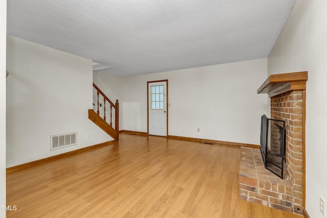 unfurnished living room with light wood finished floors, stairs, a textured ceiling, baseboards, and a fireplace