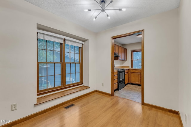 unfurnished dining area featuring light wood-style flooring, a chandelier, baseboards, and a textured ceiling