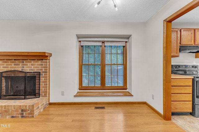 unfurnished living room featuring light wood-style floors, a textured ceiling, baseboards, and a fireplace