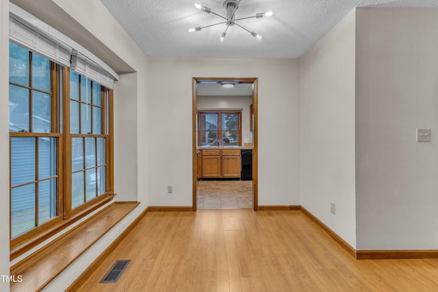 empty room with a chandelier, light wood-type flooring, baseboards, a textured ceiling, and a sink