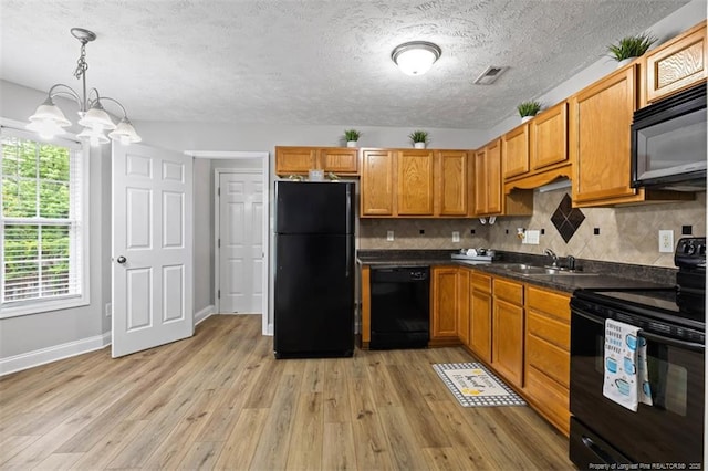 kitchen with black appliances, a sink, light wood-style flooring, dark countertops, and backsplash