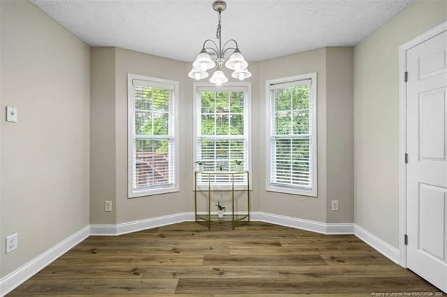 unfurnished dining area with plenty of natural light, a chandelier, baseboards, and wood finished floors