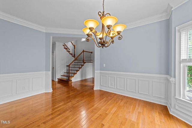 unfurnished dining area featuring light wood-type flooring, a chandelier, stairs, crown molding, and a wainscoted wall