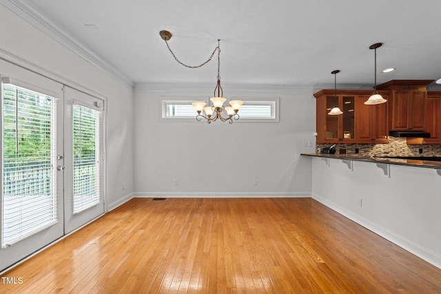 unfurnished dining area featuring a chandelier, light wood-style floors, crown molding, baseboards, and french doors