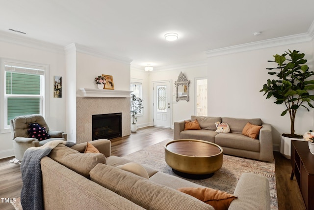 living area with wood finished floors, ornamental molding, a tiled fireplace, and baseboards