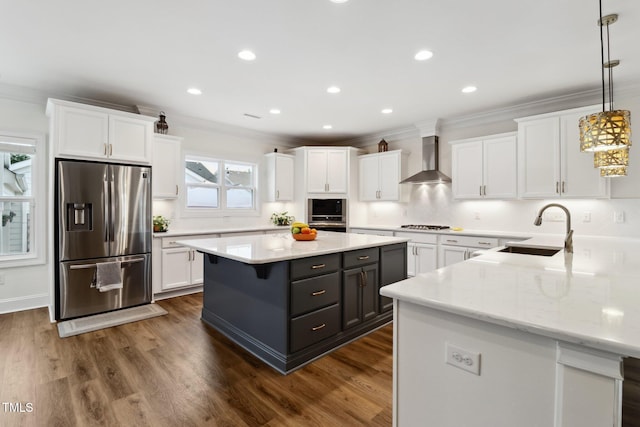 kitchen with appliances with stainless steel finishes, a sink, wall chimney range hood, white cabinetry, and crown molding
