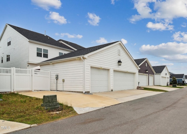 view of side of home featuring fence, driveway, and a shingled roof