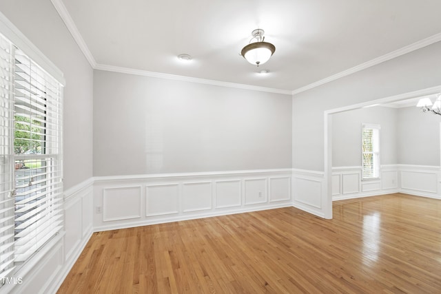 spare room featuring a chandelier, light wood finished floors, a wainscoted wall, and crown molding