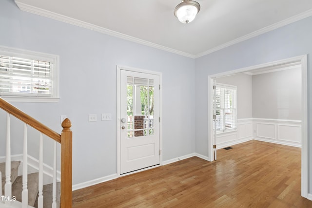 foyer featuring wood finished floors, crown molding, stairs, and a wainscoted wall