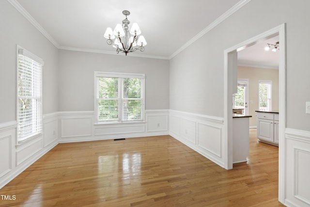 empty room featuring a chandelier, wainscoting, ornamental molding, and light wood finished floors