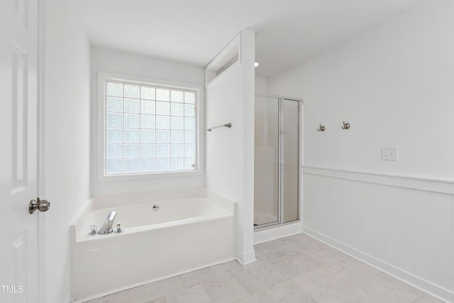 bathroom featuring a stall shower, a garden tub, wainscoting, and baseboards