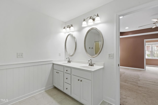 bathroom featuring a ceiling fan, double vanity, baseboards, and wainscoting