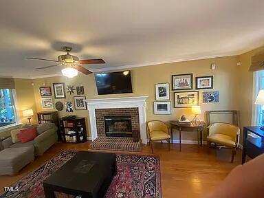 living room with a fireplace with raised hearth, wood finished floors, and a ceiling fan