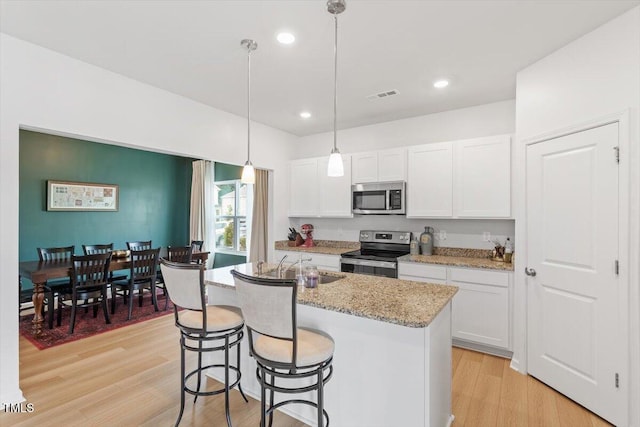 637 Marrian Dr, Clayton, NC 27520 - kitchen with stainless steel appliances, white cabinetry, a kitchen island with sink, light wood-style flooring, and recessed lighting