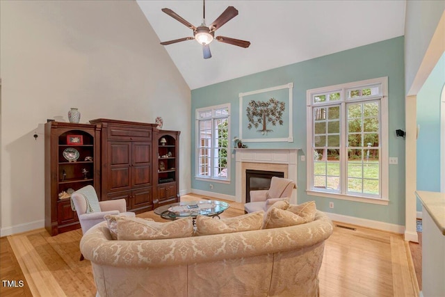 living area with high vaulted ceiling, ceiling fan, light wood-type flooring, baseboards, and a high end fireplace