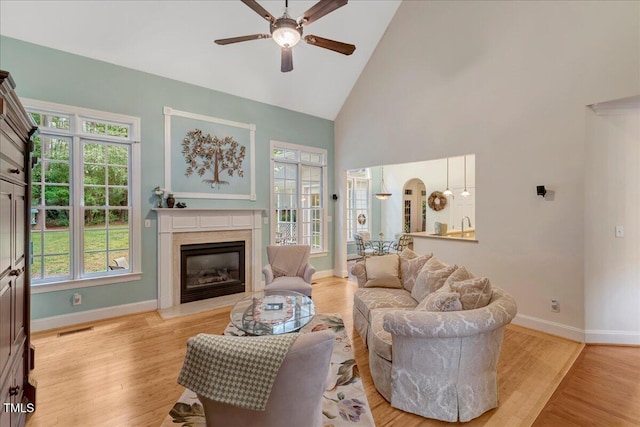 living room with ceiling fan, a high end fireplace, baseboards, high vaulted ceiling, and healthy amount of natural light