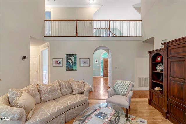 living area featuring arched walkways, a high ceiling, light wood finished floors, and crown molding