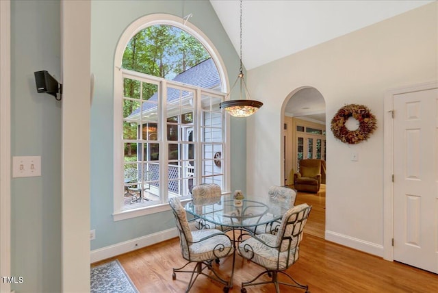 dining space featuring arched walkways, high vaulted ceiling, baseboards, and light wood-style floors