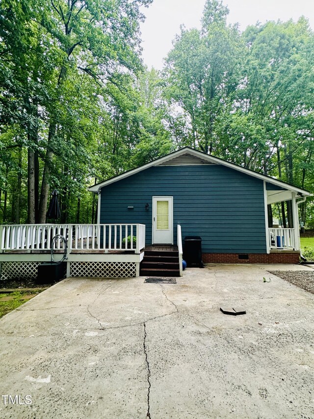 back of property featuring a wooden deck, covered porch, and view of wooded area