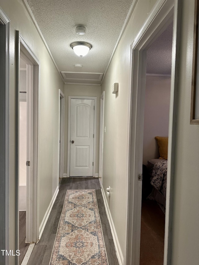 corridor with a textured ceiling, dark wood-style floors, crown molding, and baseboards