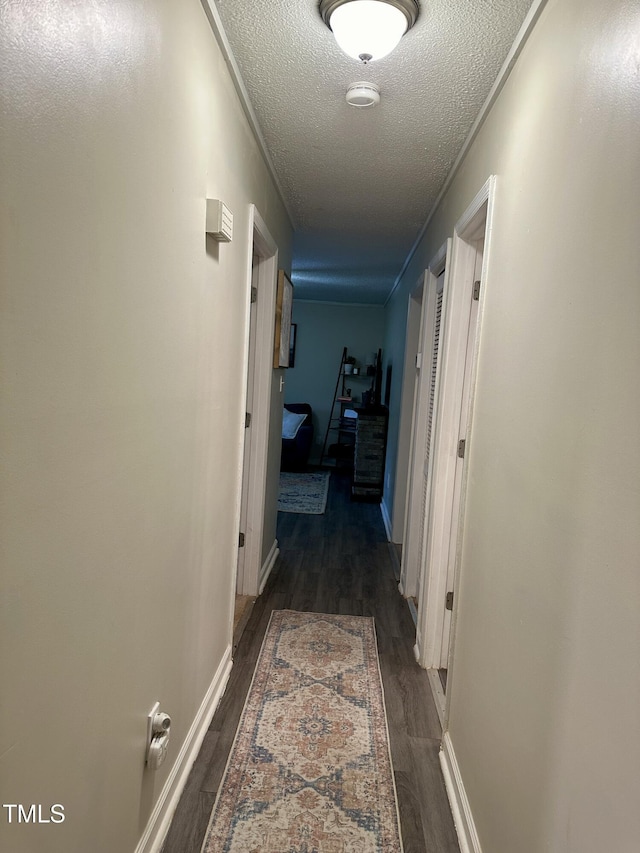 hall featuring a textured ceiling, wood finished floors, and baseboards