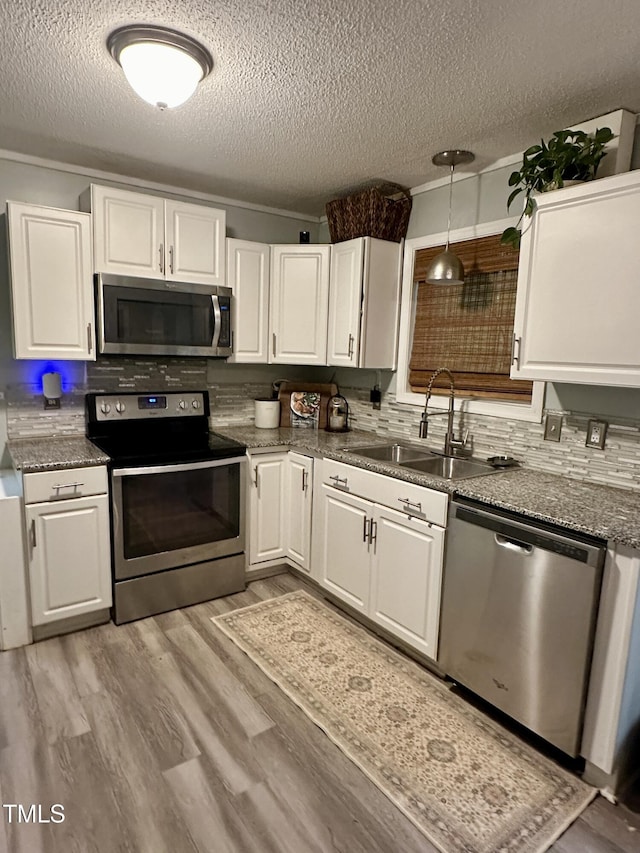 kitchen with stainless steel appliances, a sink, a textured ceiling, and white cabinetry