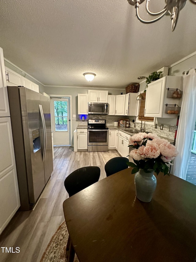 kitchen featuring stainless steel appliances, light wood-type flooring, a textured ceiling, white cabinetry, and a sink