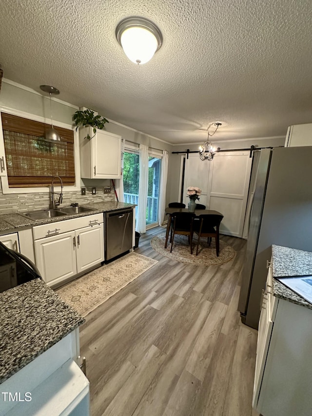 kitchen with stainless steel appliances, a textured ceiling, light wood-type flooring, a sink, and white cabinets