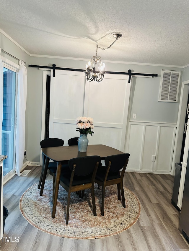 dining area with a barn door, a decorative wall, wood finished floors, a textured ceiling, and ornamental molding