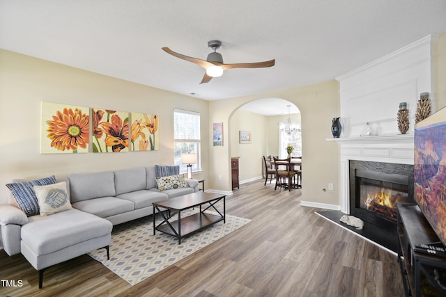 living room with arched walkways, wood finished floors, ceiling fan, baseboards, and a fireplace