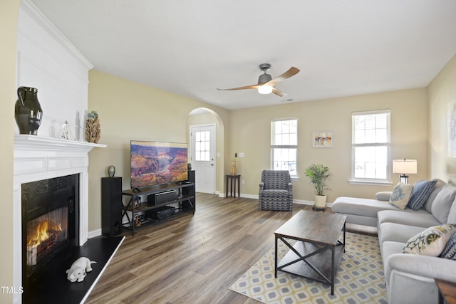 living room with a ceiling fan, a large fireplace, wood finished floors, baseboards, and arched walkways
