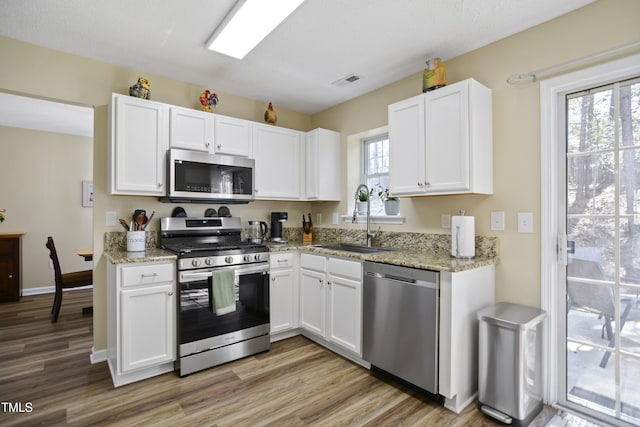 kitchen with stainless steel appliances, a sink, white cabinets, and light wood-type flooring
